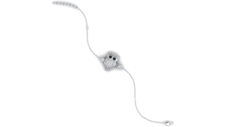 A delicate silver chain bracelet featuring a central owl charm embellished with clear diamond and small black eye accents, set against a plain white background.