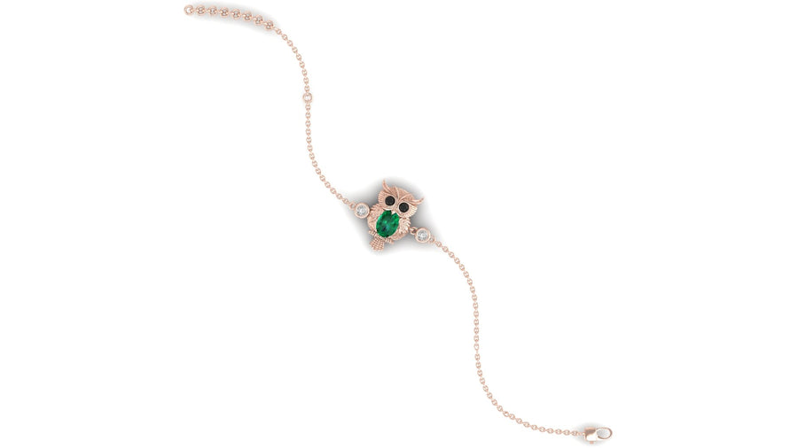 A delicate rose gold chain bracelet featuring a central owl charm with a green emerald for an eye and small clear stones, displayed on a solid white background.