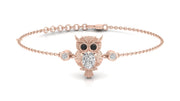 A delicate rose gold chain bracelet featuring an owl pendant with black eyes and a central clear diamond gemstone, flanked by two small round clear stones, shown on a white background.