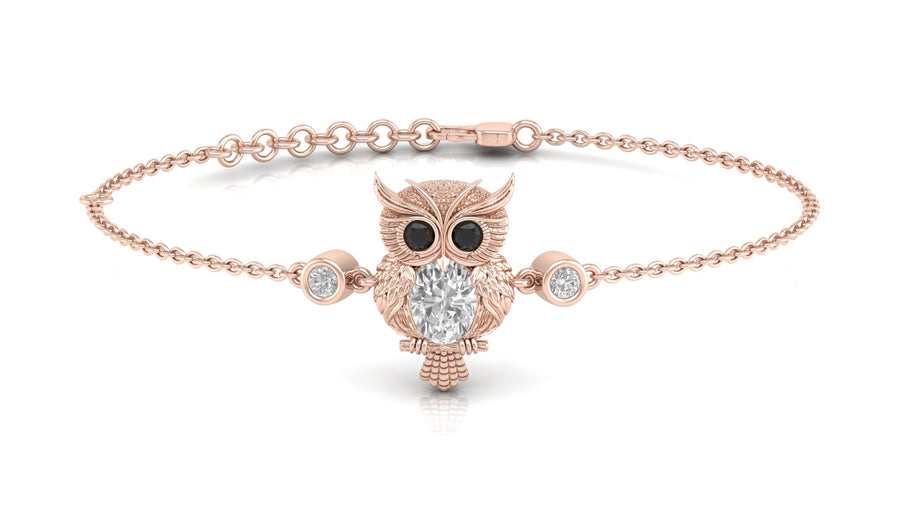 A delicate rose gold chain bracelet featuring an owl pendant with black eyes and a central clear diamond gemstone, flanked by two small round clear stones, shown on a white background.