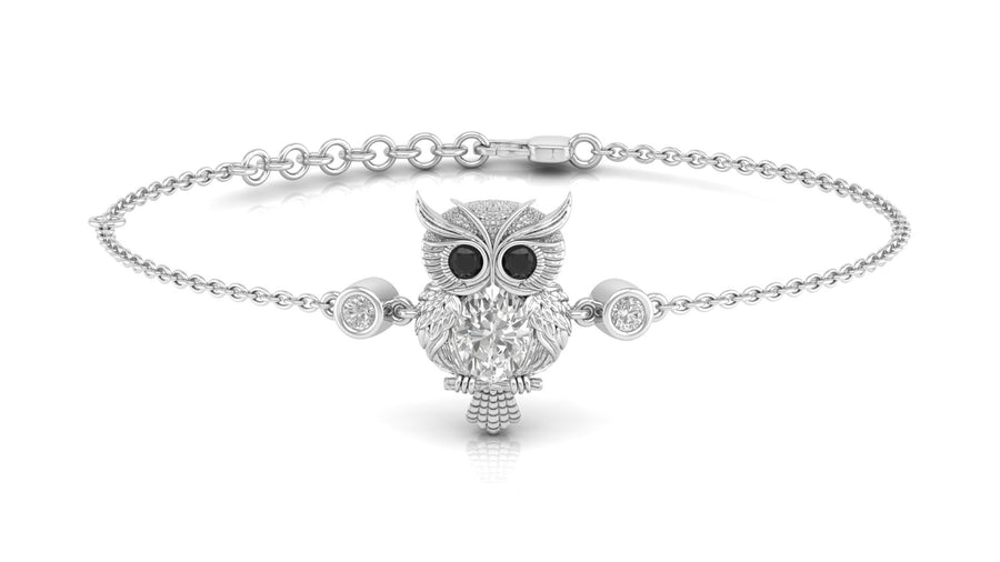 A silver chain bracelet featuring a central owl pendant with a textured silver body, black eyes, and a bright diamond gemstone detail, flanked by two small round bezel-set clear stones, shown on a white background.