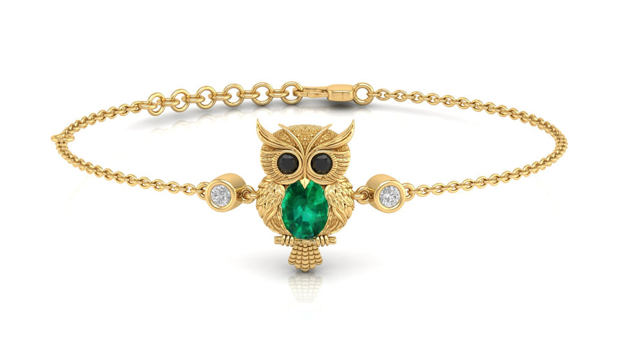 A gold chain bracelet featuring a central owl pendant with a green emerald-cut chest, black eyes, and small clear accent stones on either side, shown on a white background.