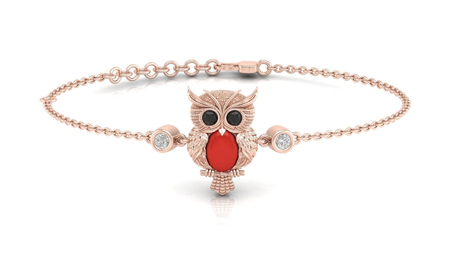 A delicate rose gold chain bracelet featuring a central owl pendant with a vibrant red coral gemstone, black eyes, and small clear accent stones on either side of the chain, set against a clean white background.