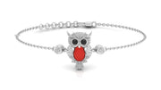 A silver chain bracelet featuring a central owl pendant with a textured silver body, black eyes, and a bright red coral gemstone detail, flanked by two small round bezel-set clear stones, shown on a white background.