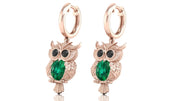 Rose gold owl earrings with green gemstones on a white background
