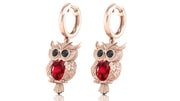 Rose gold owl earrings with ruby gemstones on a white background