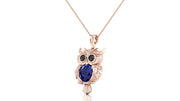 A rose gold owl pendant necklace featuring a large dark blue sapphire oval gemstone on the chest, set against a plain white background.
