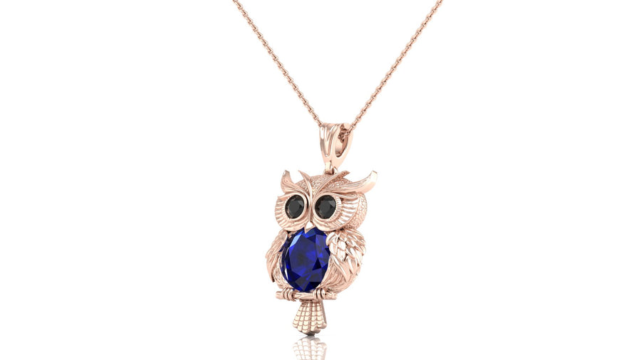 A rose gold owl pendant necklace featuring a large dark blue sapphire oval gemstone on the chest, set against a plain white background.