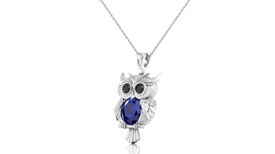 A white gold owl pendant necklace featuring a large dark blue sapphire oval gemstone in its chest, displayed on a clean white background.