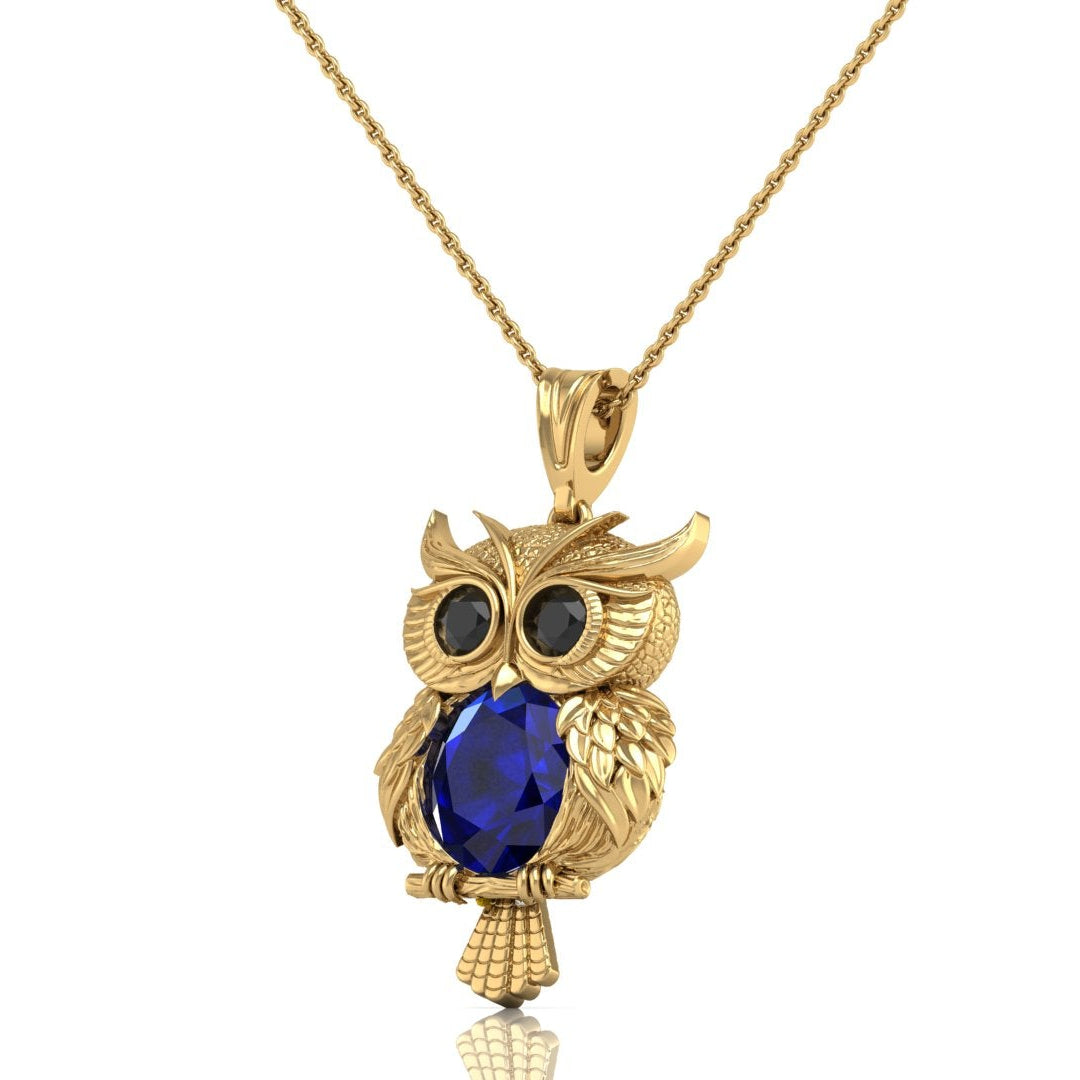 Gold owl pendant necklace with a large blue sapphire gemstone on the chest and black stone eyes, shown on a white background.