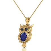 Gold owl pendant necklace with a large blue sapphire gemstone on the chest and black stone eyes, shown on a white background.