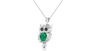 A white gold owl pendant necklace featuring a large emerald oval gemstone on the chest and black stone eyes, suspended from a delicate silver chain against a white background.