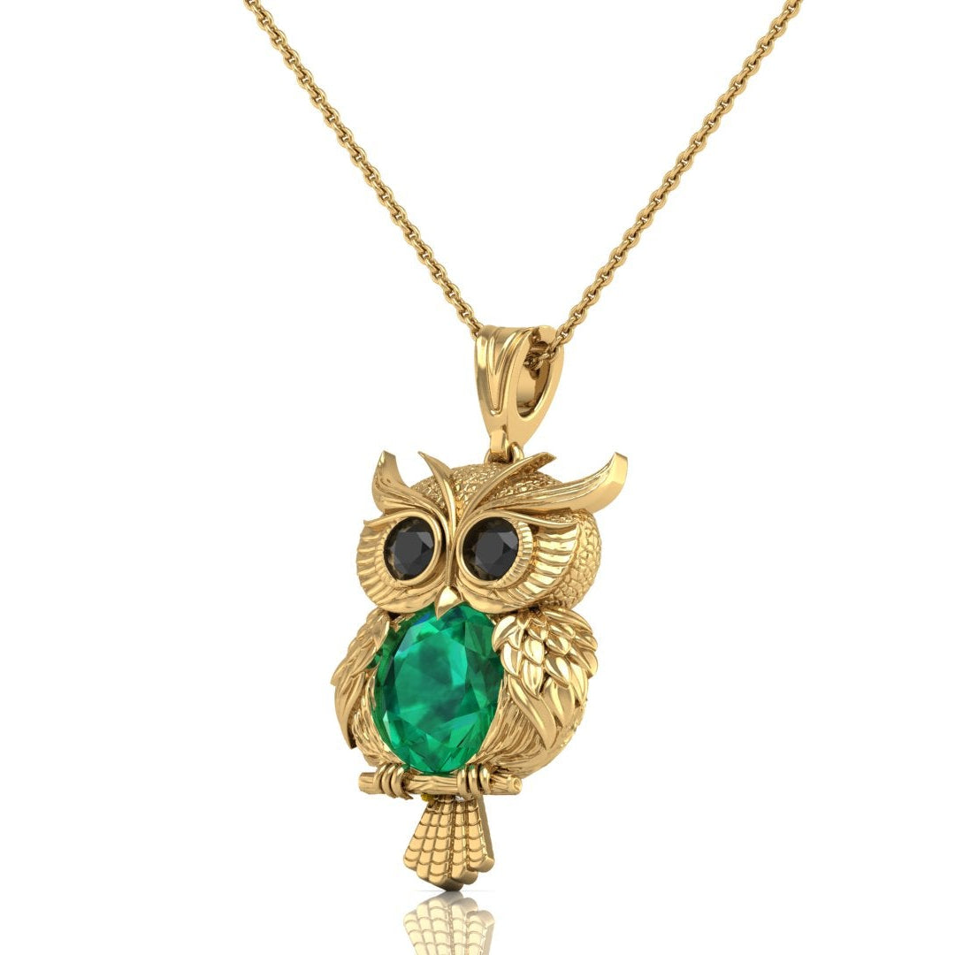 A gold owl pendant necklace featuring a large green emerald oval cut stone in the center and black stone eyes, hanging from a gold chain against a white background.