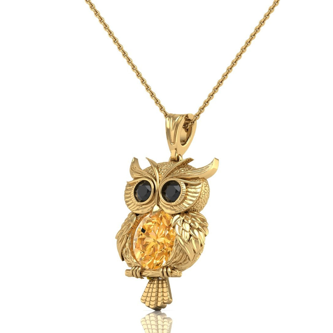 A gold owl pendant necklace featuring a large round yellow sapphire center stone and dark round eyes, suspended from a delicate gold chain against a white background.