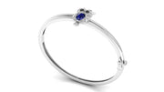 A white gold bangle bracelet featuring a small owl charm with a Blue sapphire centrestone and dark eyes, set against a plain white background.