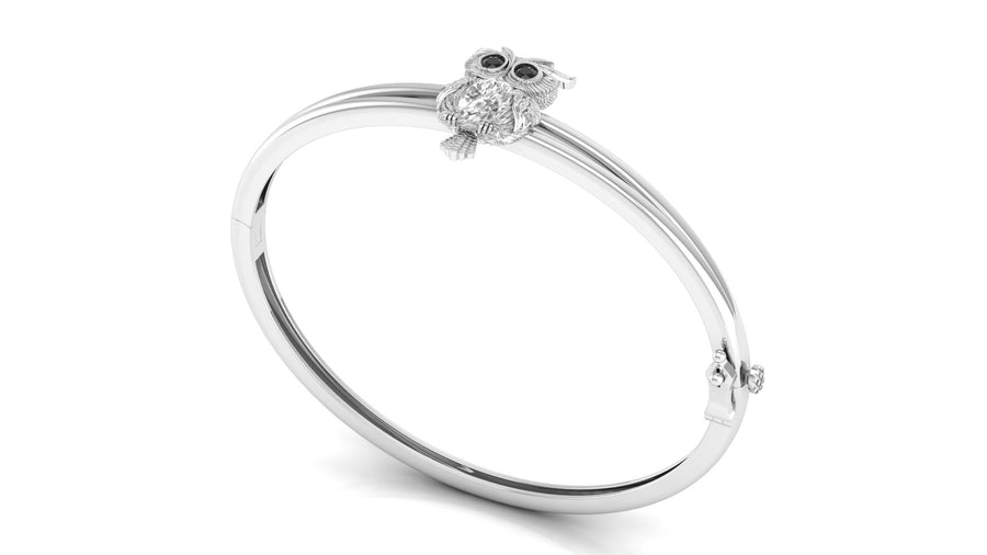 A polished white gold bangle bracelet featuring a small owl charm with dark eyes and clear stones, shown on a clean white background.