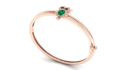 A rose gold bangle bracelet featuring a small owl charm with a green heart-shaped gemstone and dark eyes, set against a clean white background.