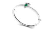 A white gold bangle bracelet featuring a small owl charm with a green emerald gemstone and black eyes, displayed on a clean white background.