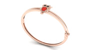 A rose gold bangle bracelet featuring a small owl charm with a red coral centre stone and black eyes, set against a plain white background.