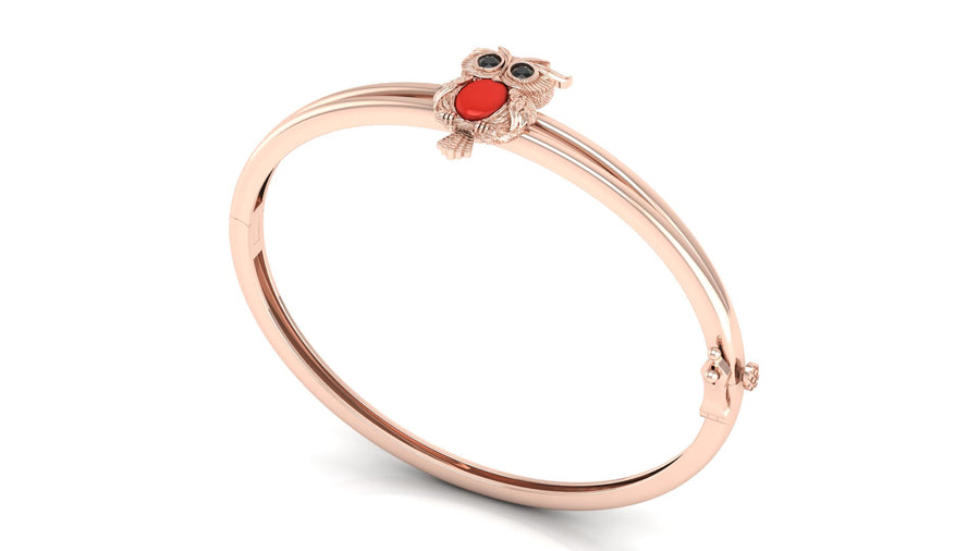 A rose gold bangle bracelet featuring a small owl charm with a red coral centre stone and black eyes, set against a plain white background.