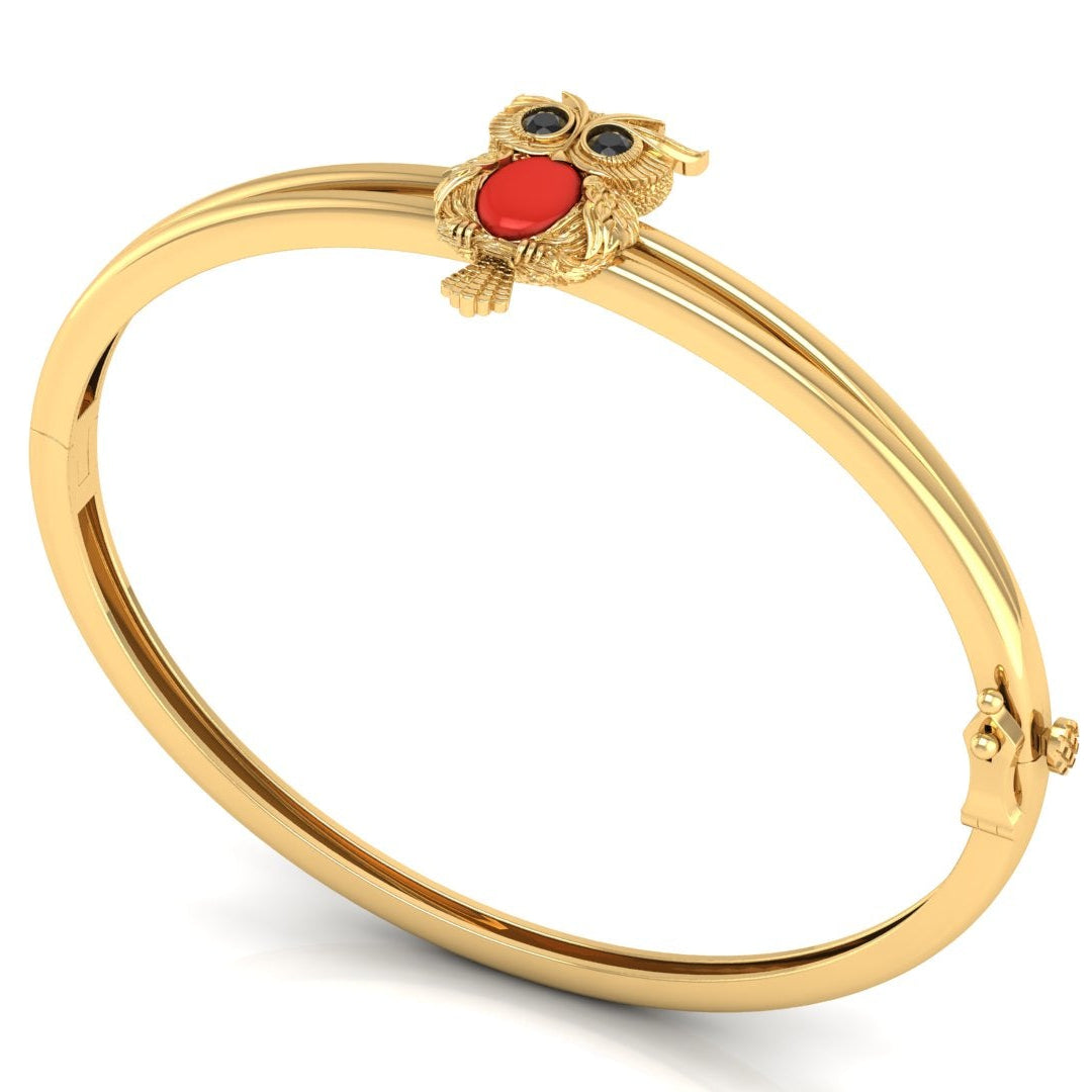 A gold bangle bracelet featuring a small owl charm with a red coral centre centrepiece and dark eyes, displayed on a clean white background.