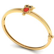A gold bangle bracelet featuring a small owl charm with a red coral centre centrepiece and dark eyes, displayed on a clean white background.