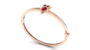 A rose gold bangle bracelet featuring a small owl charm with a red ruby centrestone and black eyes, set against a plain white background.