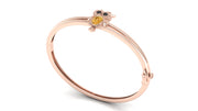 A rose gold bangle bracelet featuring a small owl charm with a yellow sapphire gemstone face and black eyes, set against a plain white background.