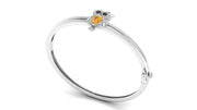 A white gold bangle bracelet featuring a small owl charm with a yellow sapphire centrestone and dark eyes, set against a plain white background.