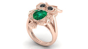 Rose gold ring with emerald and black gemstones on a white background