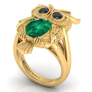 Gold owl-shaped ring with green gemstone and black stones on a white background