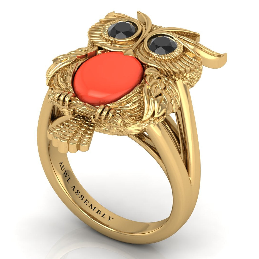 Gold owl-shaped ring with red coral gemstone and black stones on a white background