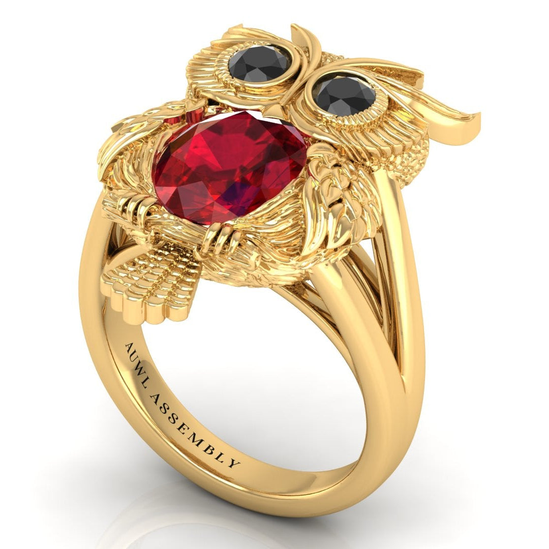 Gold owl-shaped ring with ruby gemstone and black stones on a white background