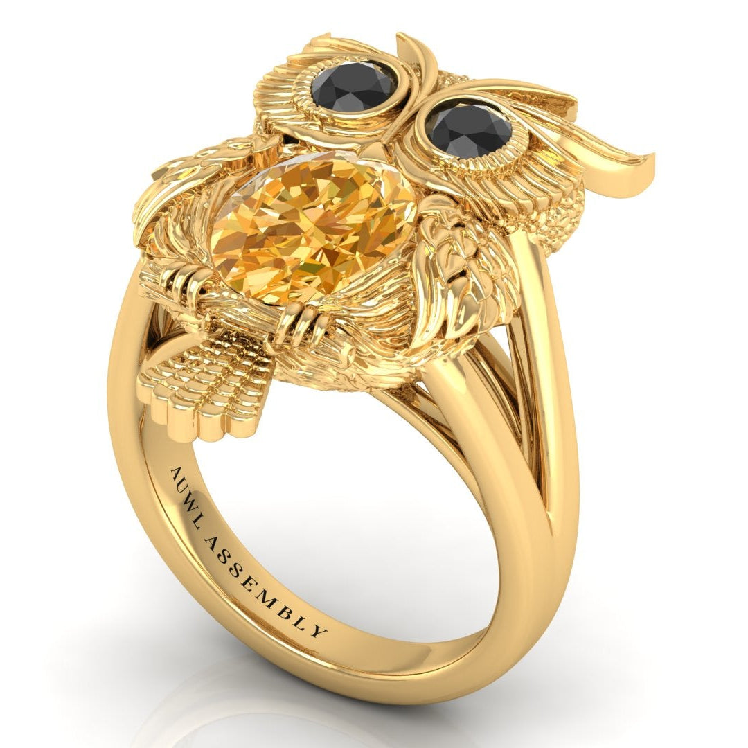 Gold owl-shaped ring with yellow sapphire gemstone and black stones on a white background