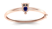 A rose gold bangle bracelet featuring a small owl charm with a round Blue sapphire centrepiece and black eye stones, set against a clean white background.