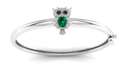 A white gold bangle bracelet featuring an owl charm with a green oval gemstone and small black stone eyes, shown on a clean white background.