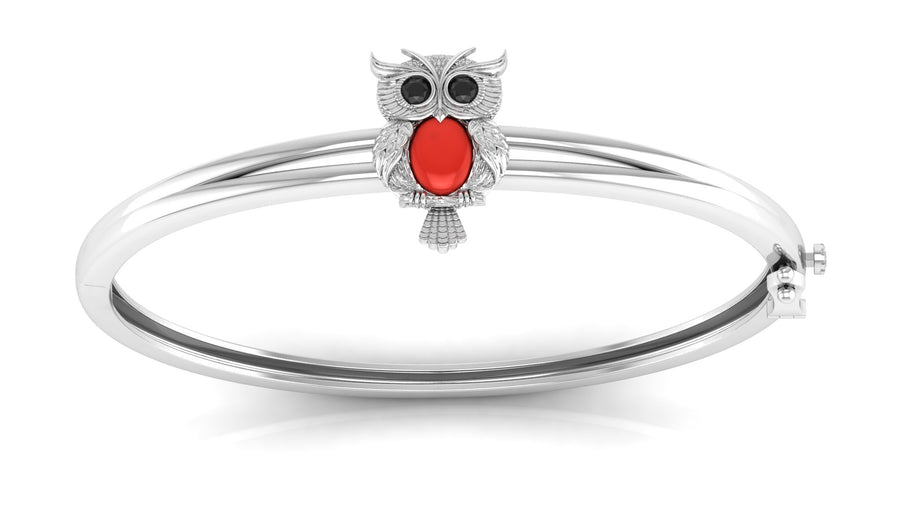 A white gold bangle bracelet featuring a small owl charm with ared coral centre stone on the front, set against a plain white background.