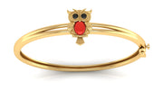 Gold bangle bracelet featuring an owl charm with a red coral centre stone and black eyes, set against a plain white background.
