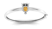 A white gold bangle bracelet featuring a small owl charm with a round yellow sapphire gemstone and black stone eyes, set against a plain white background.