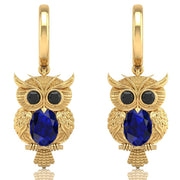 Gold owl earrings with blue sapphire gemstones on a white background