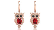 Rose gold owl earrings with ruby gemstones on a white background