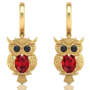 Gold owl earrings with ruby gemstones on a white background