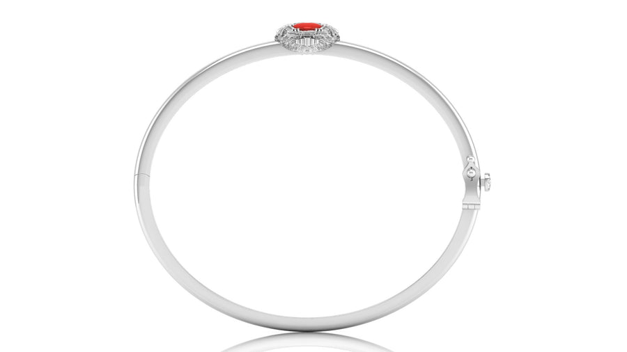 A polished white gold bangle bracelet with a small oval red coral centre stone  and surrounding clear stones at the top, shown on a plain white background.