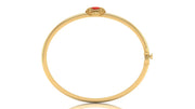 A gold bangle bracelet with a small red coral centre stone and gold detailing at the top, shown on a plain white background.