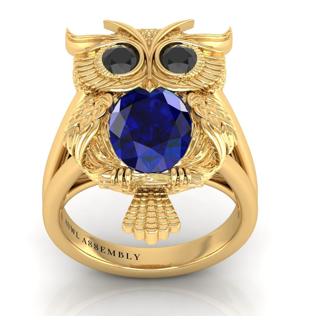 Gold owl-shaped ring with a blue sapphire gemstone on a white background