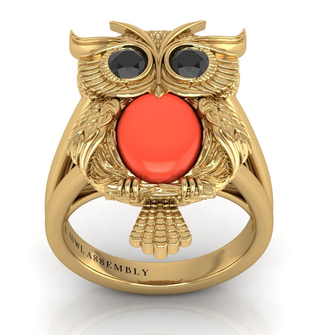 Gold owl-shaped ring with a red coral gemstone on a white background