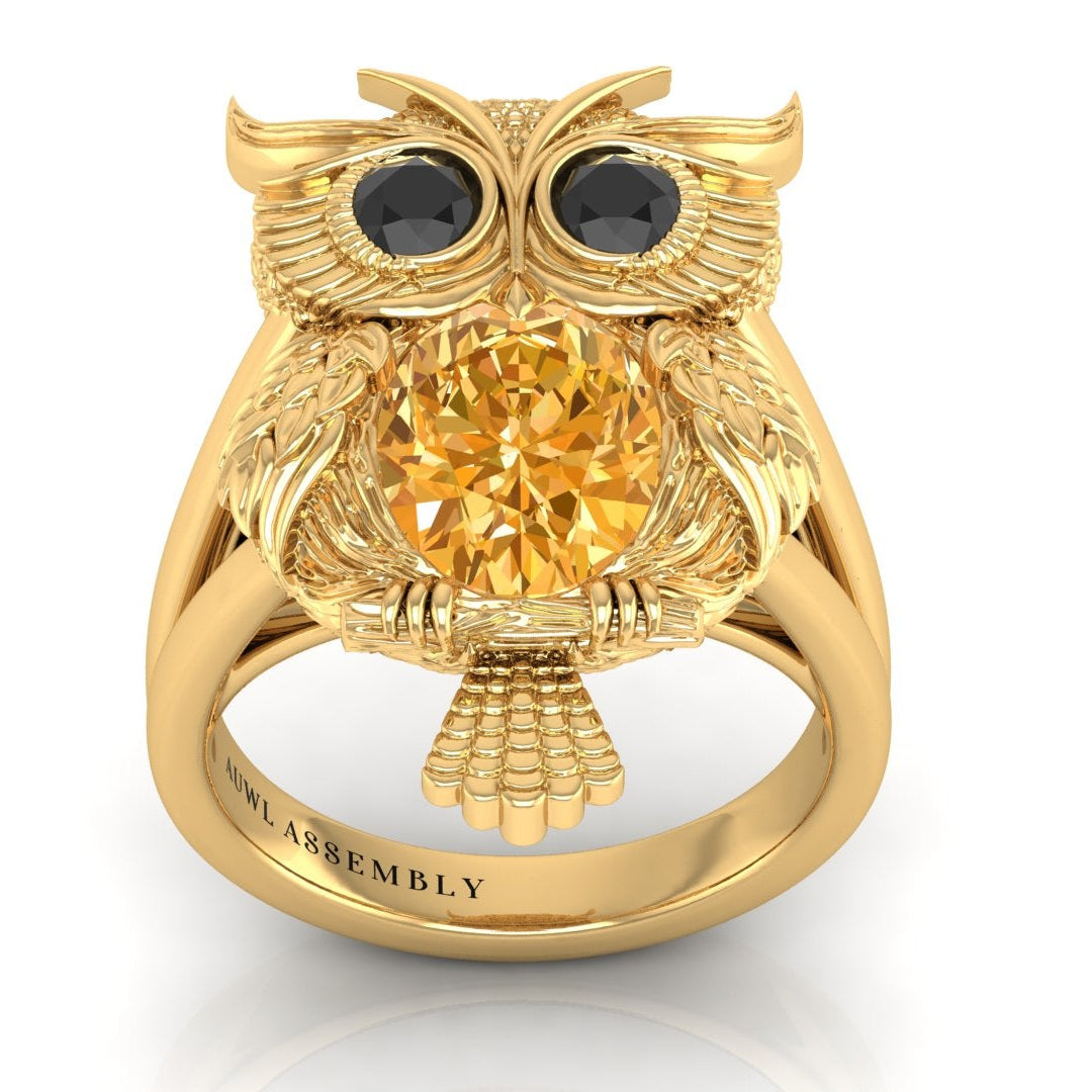 Gold owl-shaped ring with a yellow sapphire gemstone on a white background