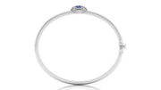 A polished white circular bangle bracelet with a small oval Blue sapphire gemstone and surrounding clear stones at the top, shown on a white background.