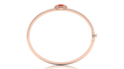 A slim rose gold bangle bracelet with a small red coral centre stone and clear accent stones at the clasp, shown on a white background with a soft reflection.