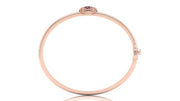 A slim rose gold bangle bracelet with a small oval ruby gemstone and tiny clear accent stones at the top clasp, shown on a white background with a faint reflection.